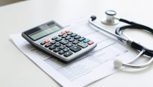 A calculator resting on a medical billing statement beside a stethoscope on a desk