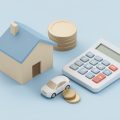 Small model house and car beside a calculator and stacked coins on a plain surface
