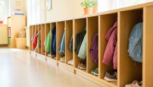 A row of children's cubbies with small coats, backpacks, and shoes in a bright daycare hallway