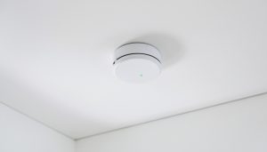 A round white smoke alarm mounted on a ceiling in a bright home